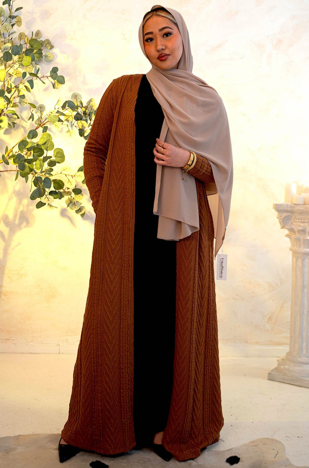 a woman wearing a brown shawl standing in front of a tree