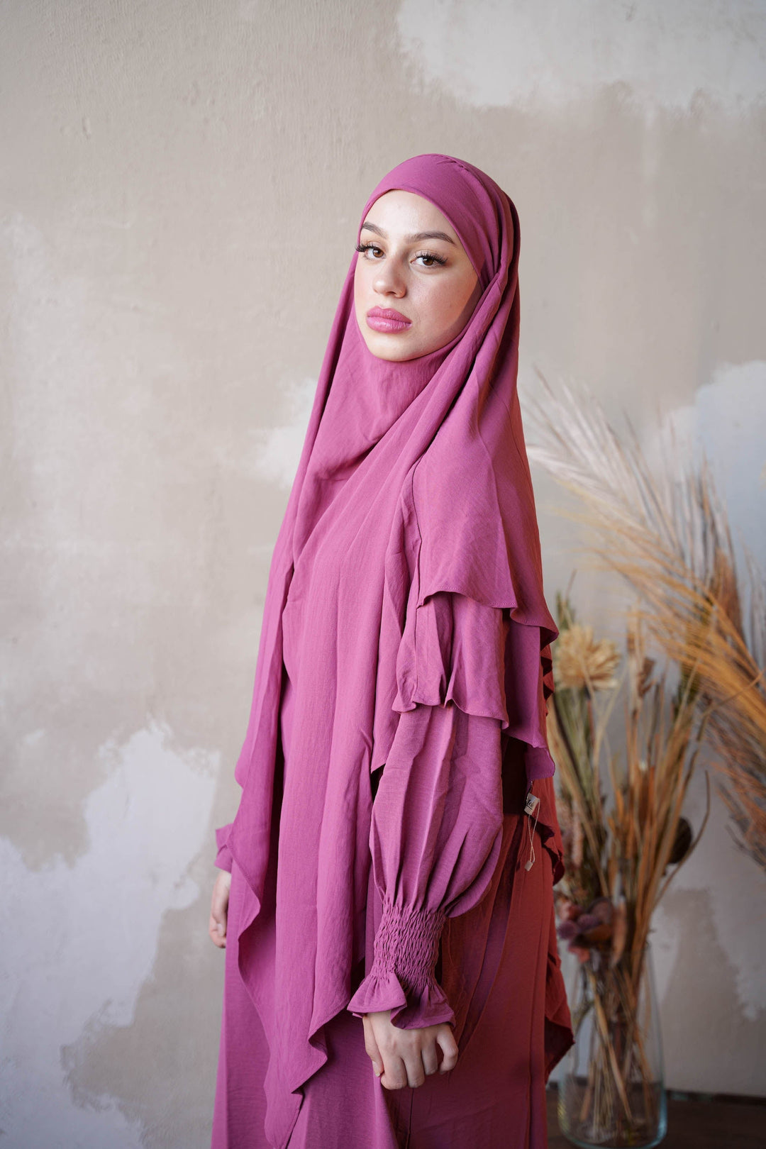 a woman wearing a purple hijab standing in front of a plant
