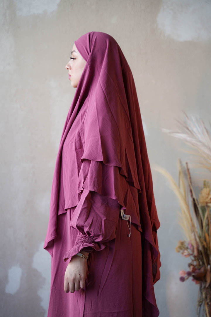 a woman in a purple hijab standing in front of a wall