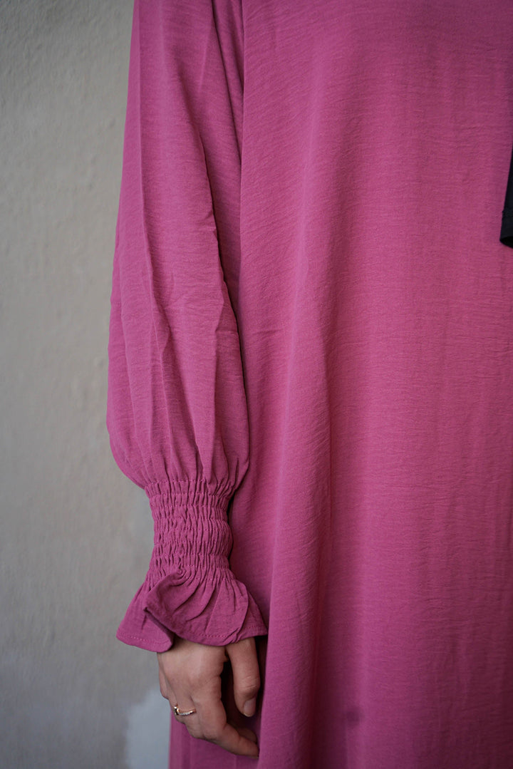 a woman in a pink shirt is holding her hand on her hip