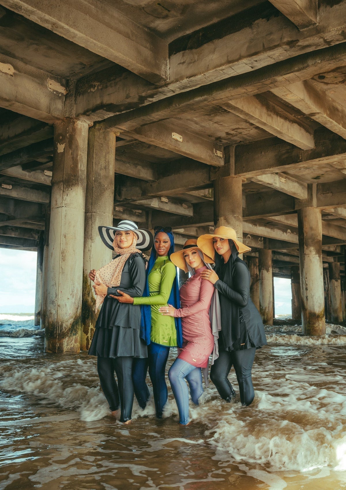 Three women wearing modest swimsuits, including burkinis, on a beach showcasing Urban Modesty's stylish full-coverage swimwear.