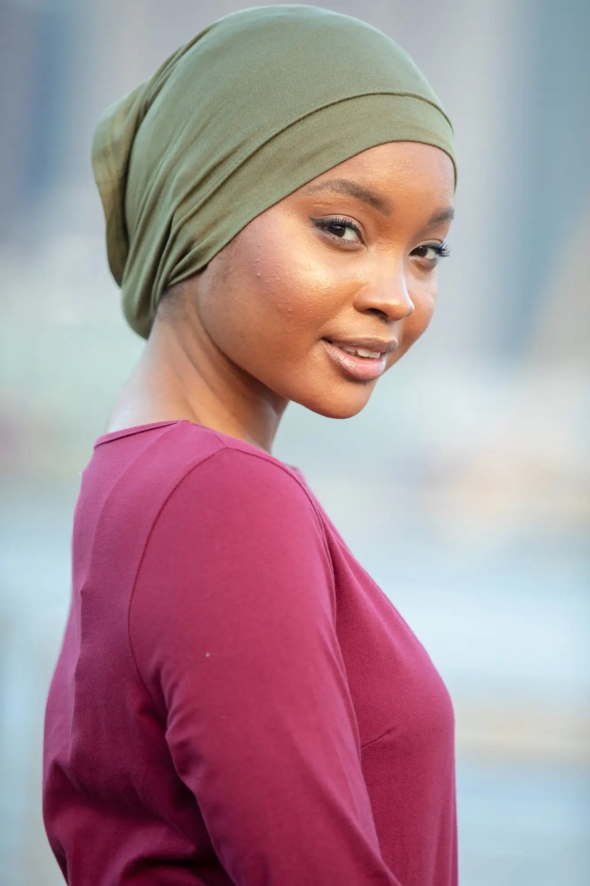 Woman wearing green Hijab Underscarves under a maroon top, outdoor backdrop