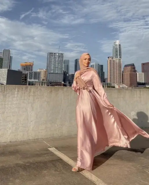 Influencers Collection featuring a trendy pink silk abaya blowing in the wind with a cityscape background, perfect for modest fashion lovers.