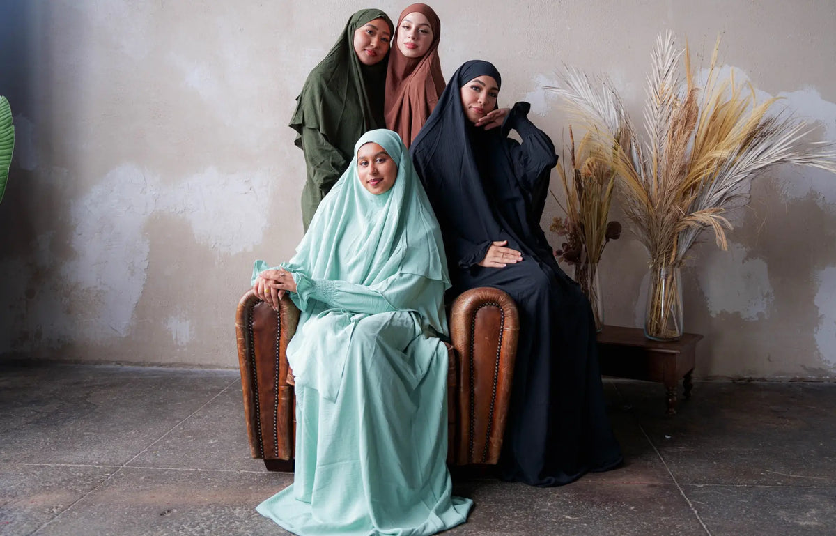 Shop Clothing & Hijab - Four women wearing diverse hijabs seated on a chair for a modern fashion photo shoot.