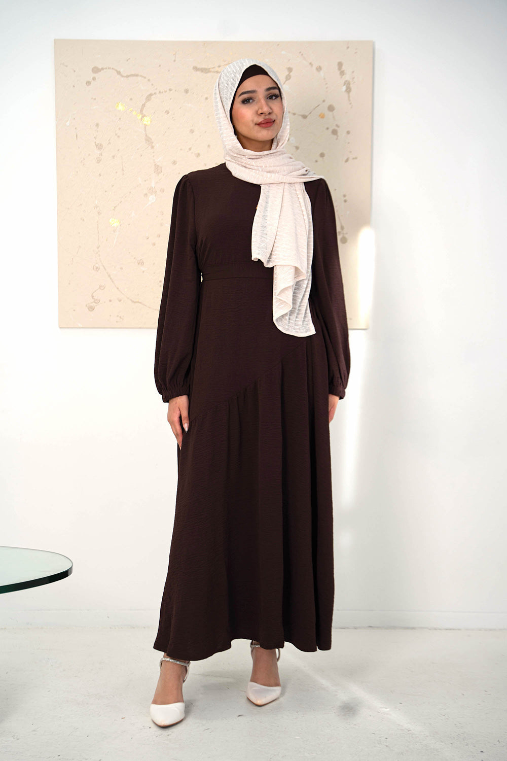 Model wearing Brown Asymmetrical Hem Maxi Dress with belt, chiffon hijab, cuff sleeves, and ruffled details, standing in modern setting.