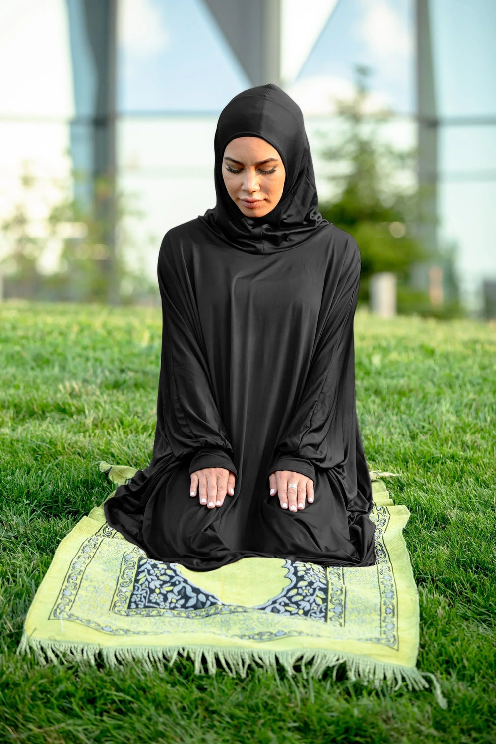 Black One Piece Salah Prayer Outfit worn outdoors with a green prayer mat on grass.