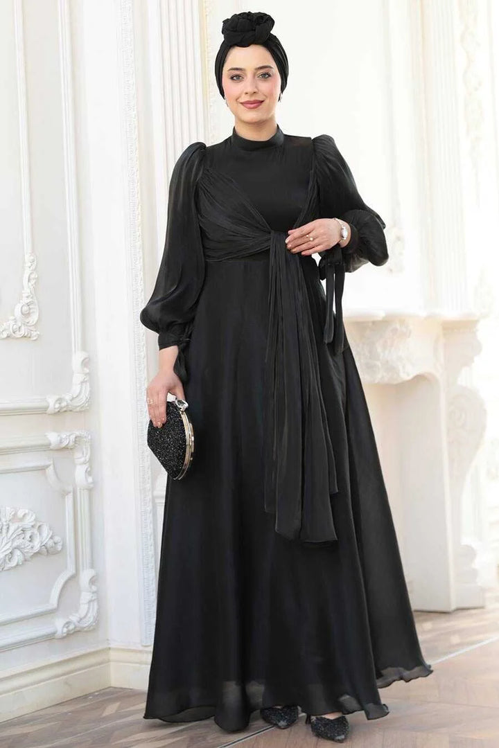 Woman wearing Black Organza Criss Cross Gown with elegant puff sleeves, holding a clutch in a chic setting.