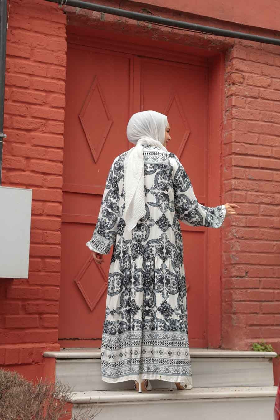 Woman in a patterned maxi dress standing on steps in front of a red brick building.