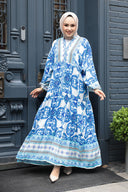 Woman in a blue and white patterned long dress with a headscarf standing in front of ornate doors.