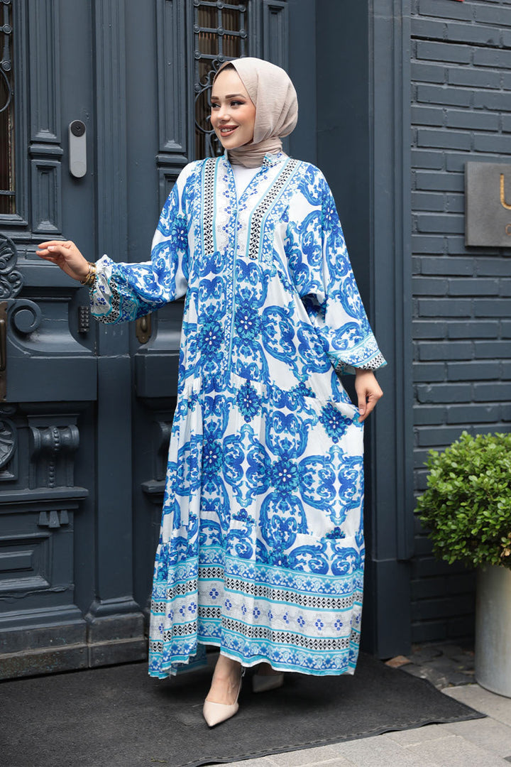 Woman wearing Blue Tropical Smocked Maxi Dress CLEARANCE with ruffle hem and elastic cuffs standing near blue door.