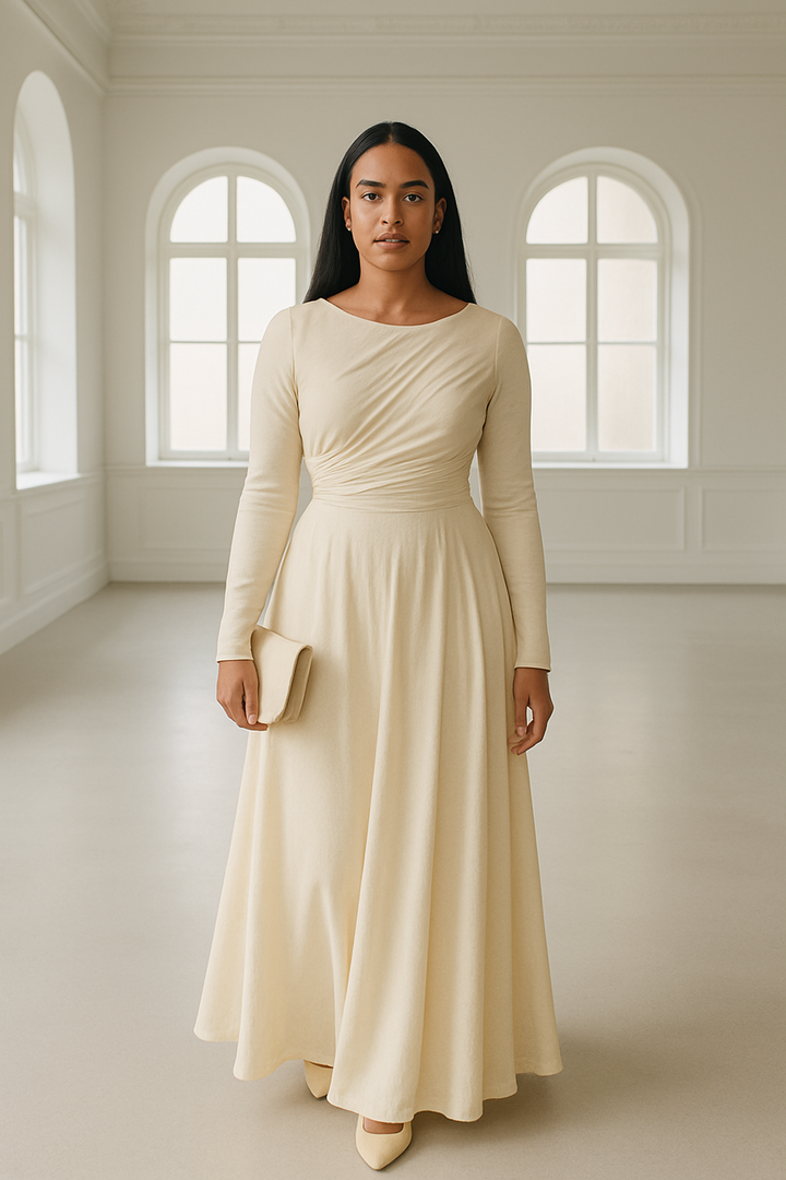 Woman wearing a beige drop waist dress standing in a bright room with arched windows.