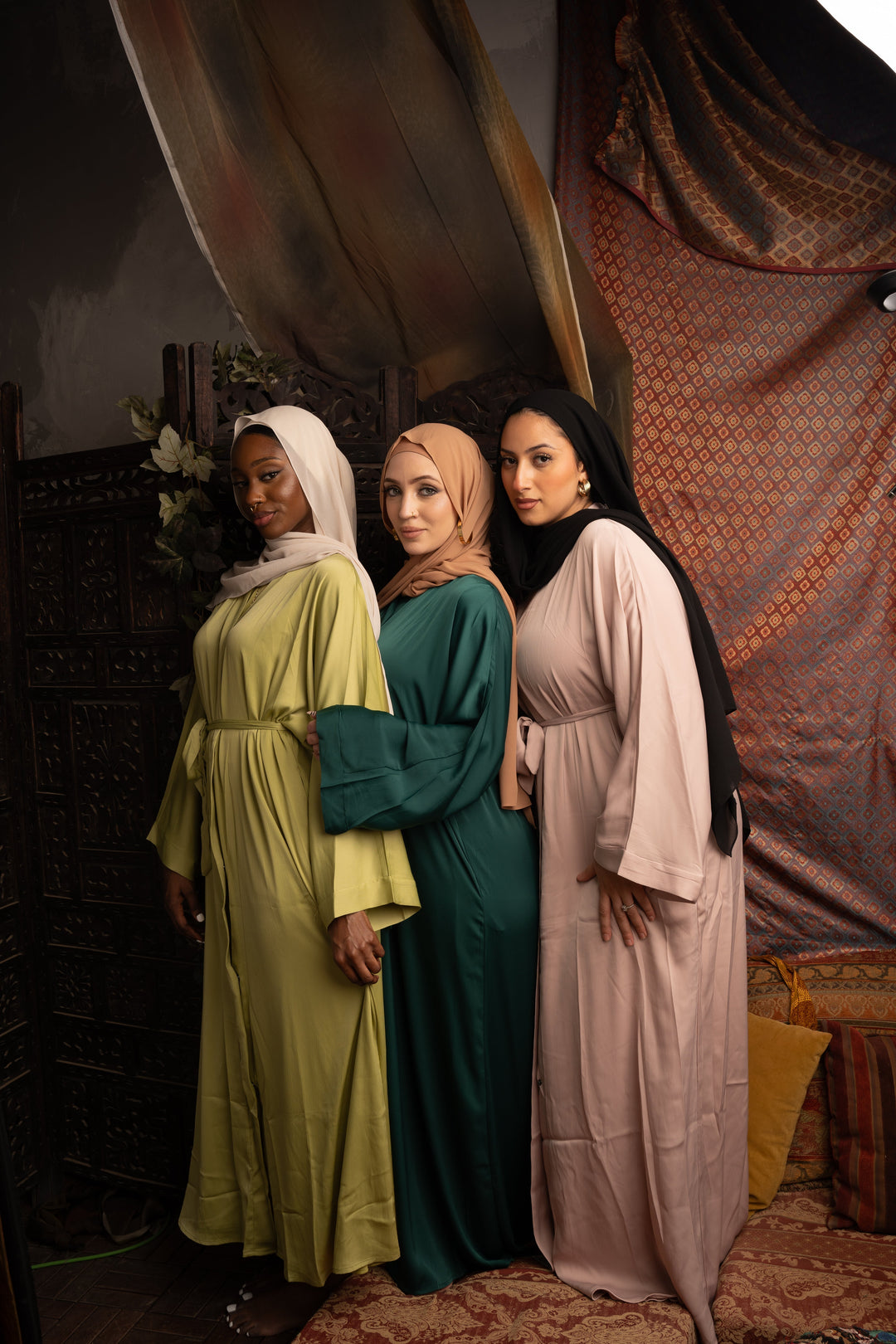 Three women wearing long sleeved modest abayas in various colors, standing together in an elegant and stylish setting.