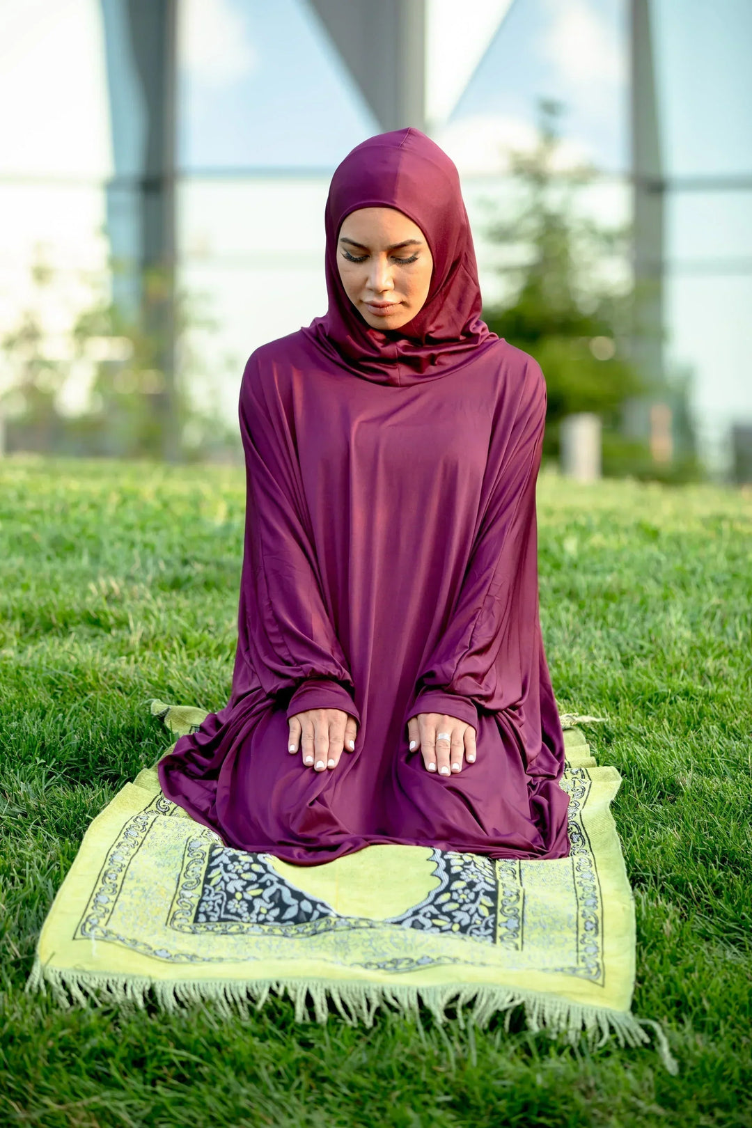 Woman wearing Maroon One Piece Salah Prayer Outfit kneeling on a prayer mat outdoors