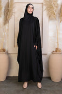 Woman wearing a black one-piece salah prayer outfit standing indoors.