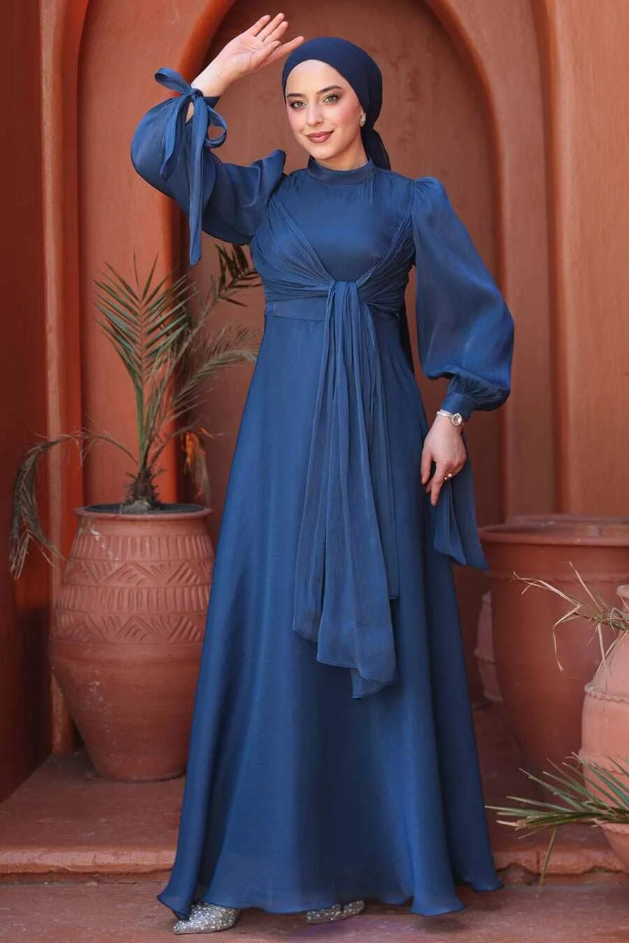 Elegant woman wearing a Navy Blue Organza Criss Cross Gown with long sleeves and a crew neckline, posing stylishly in a garden setting.