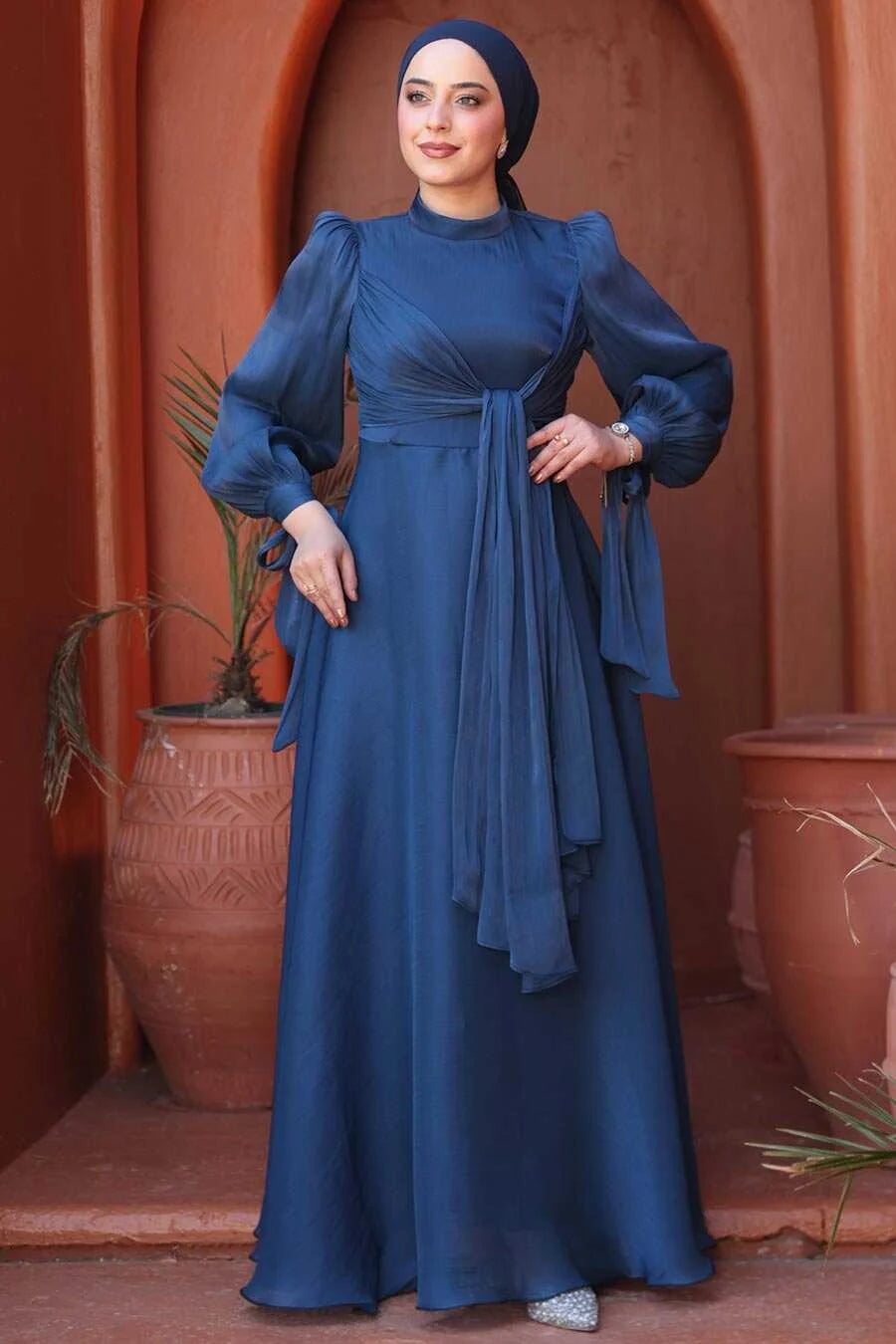 Model wearing Navy Blue Organza Criss Cross Gown with fit and flare silhouette, long sleeves, and crew neckline in elegant setting.