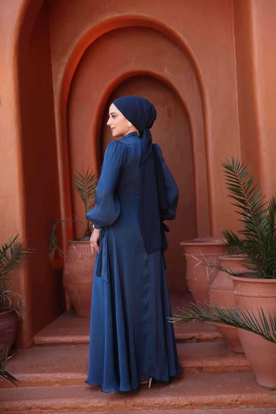 Woman wearing Navy Blue Organza Criss Cross Gown against terracotta backdrop