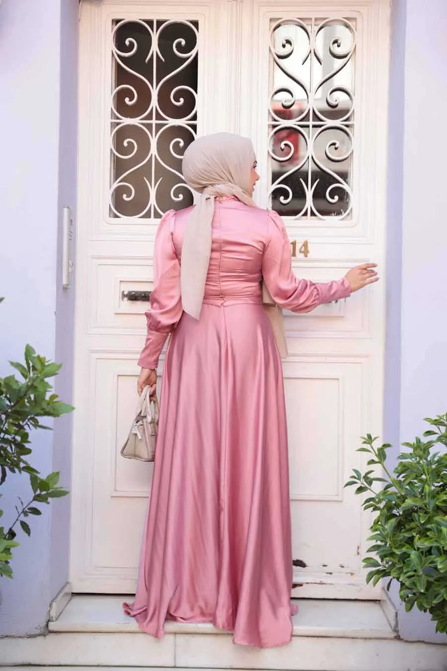 Woman in Pink Rose Satin Gown in front of white door with decorative grille
