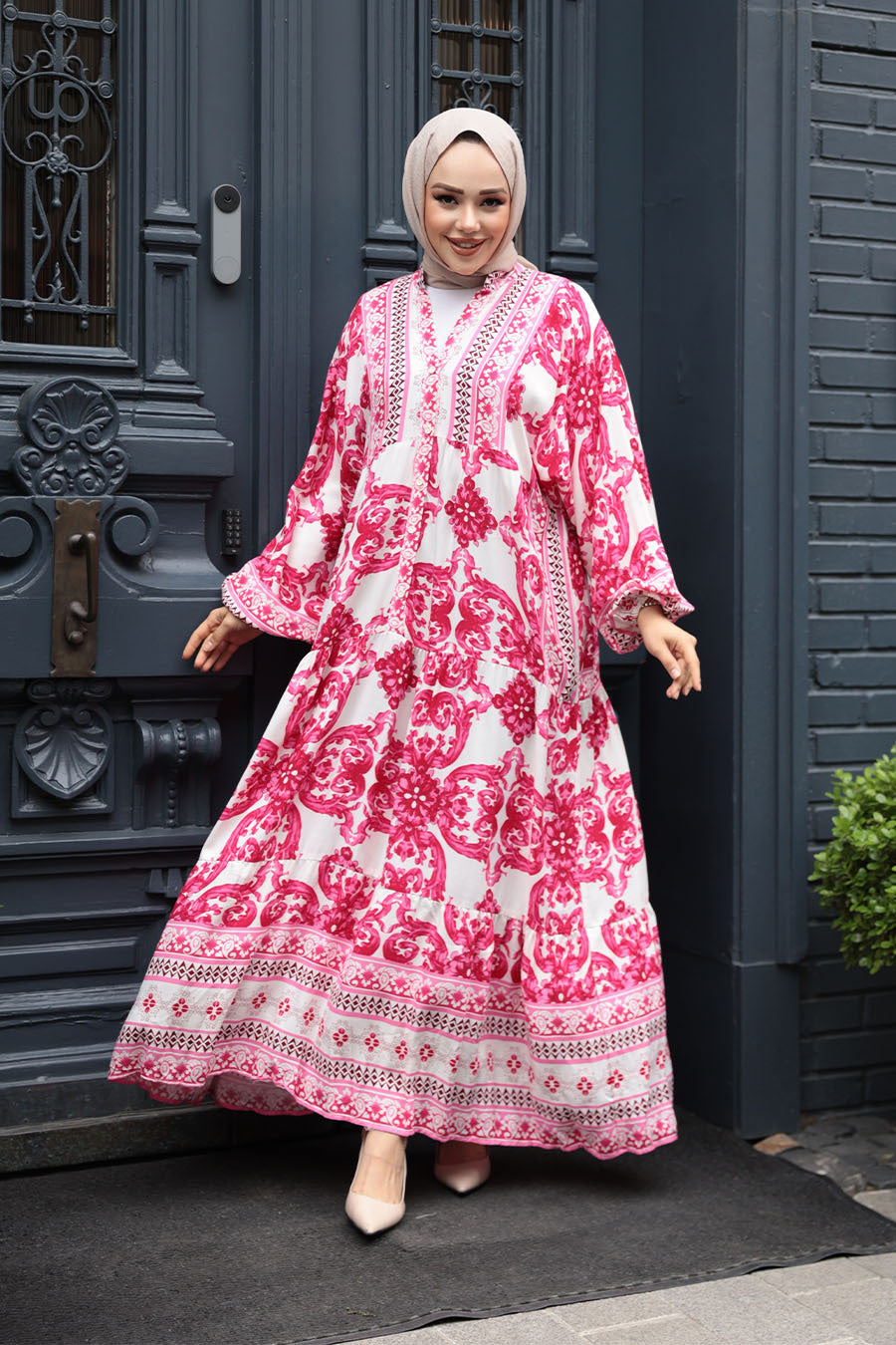Woman in a long-sleeved pink and white patterned dress standing in front of a decorative door.