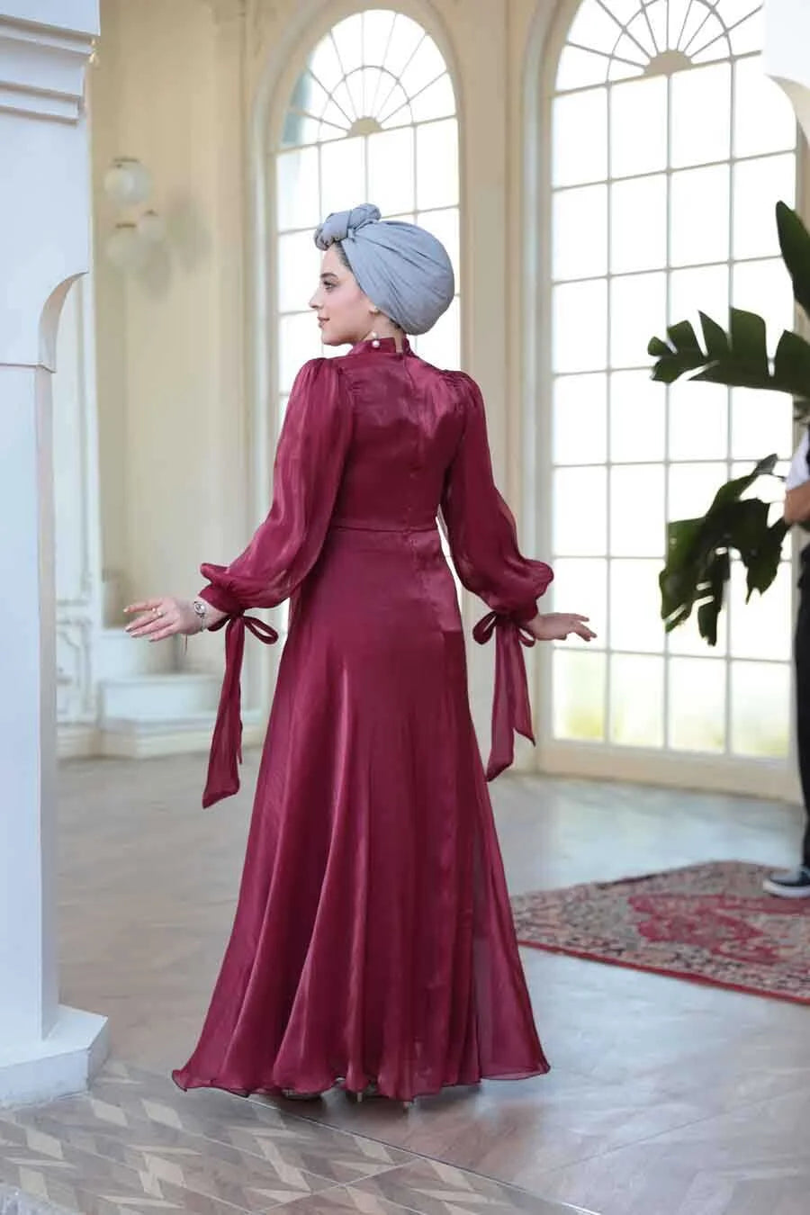 Woman wearing a Red Organza Criss Cross Gown by Urban Modesty, showcasing elegant back design with fit and flare silhouette.
