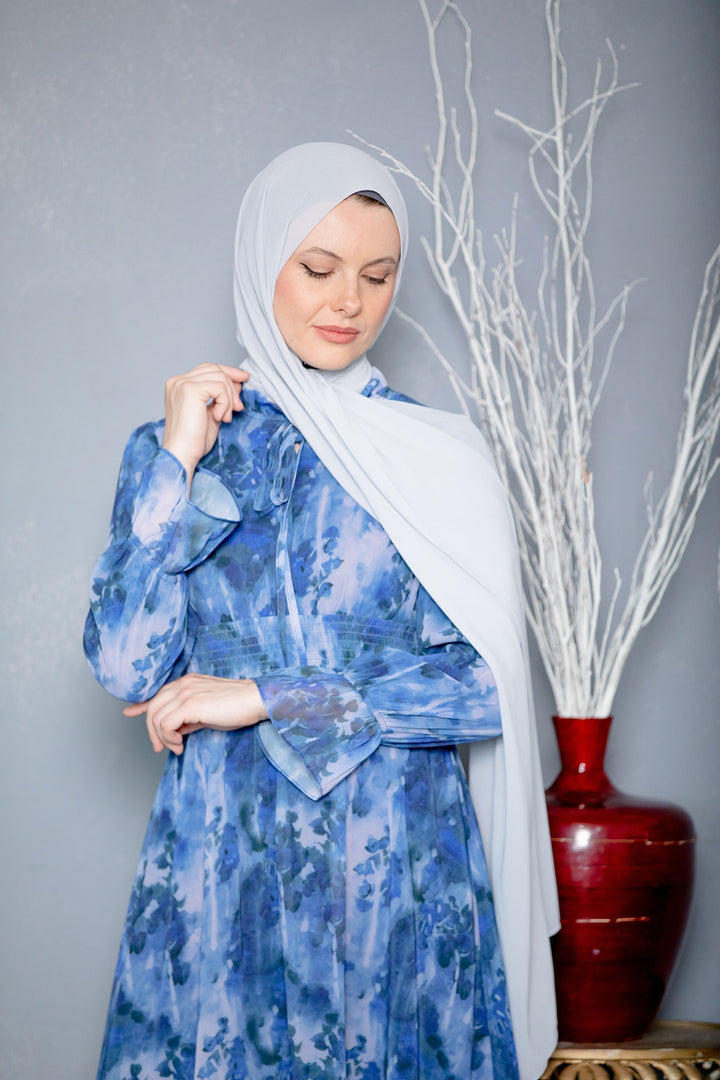 Woman in blue floral dress wearing white chiffon hijab