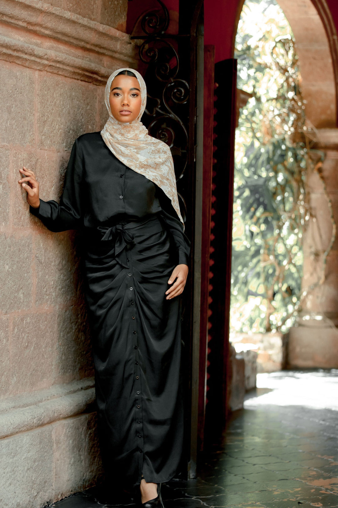 Woman in a black satin maxi dress and patterned hijab with black button skirt set