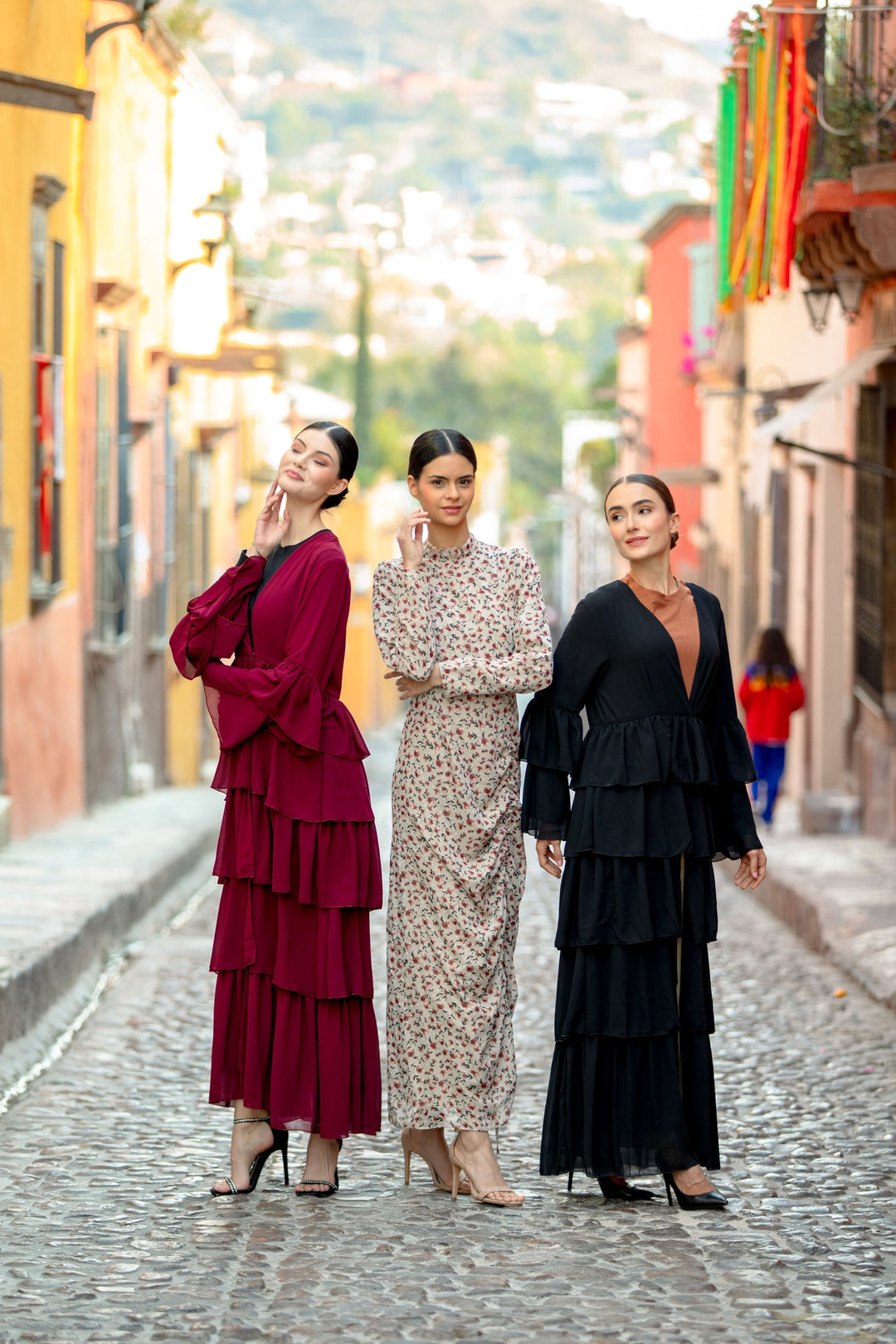 Three women in tiered dresses showcasing Black Cascading Ruffles Open Front Abaya