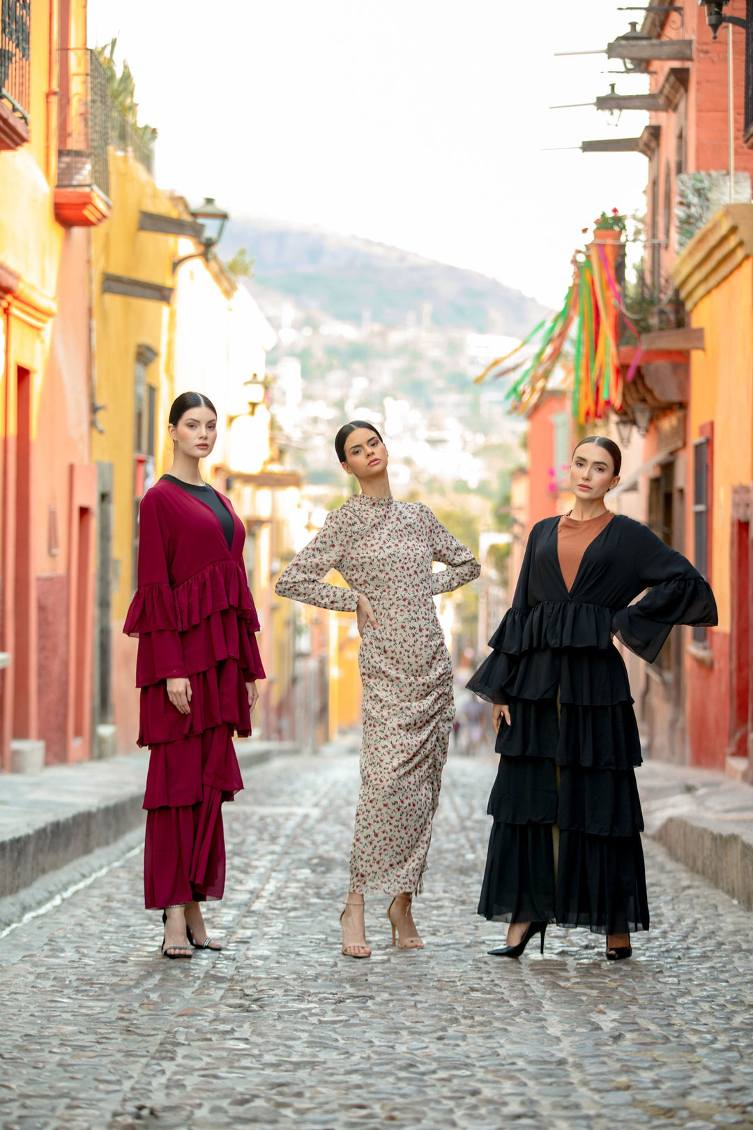 Three women showcasing the Black Cascading Ruffles Open Front Abaya with tiered ruffles