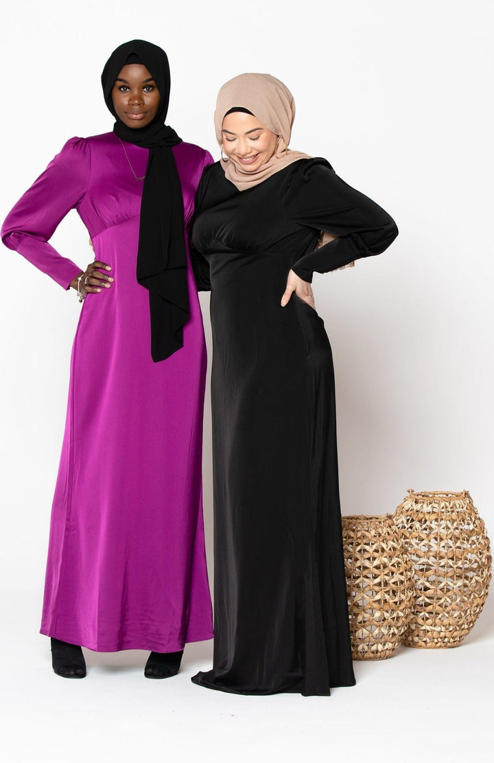 Two women in black satin long sleeve maxi dresses and hijabs, showcasing elegance