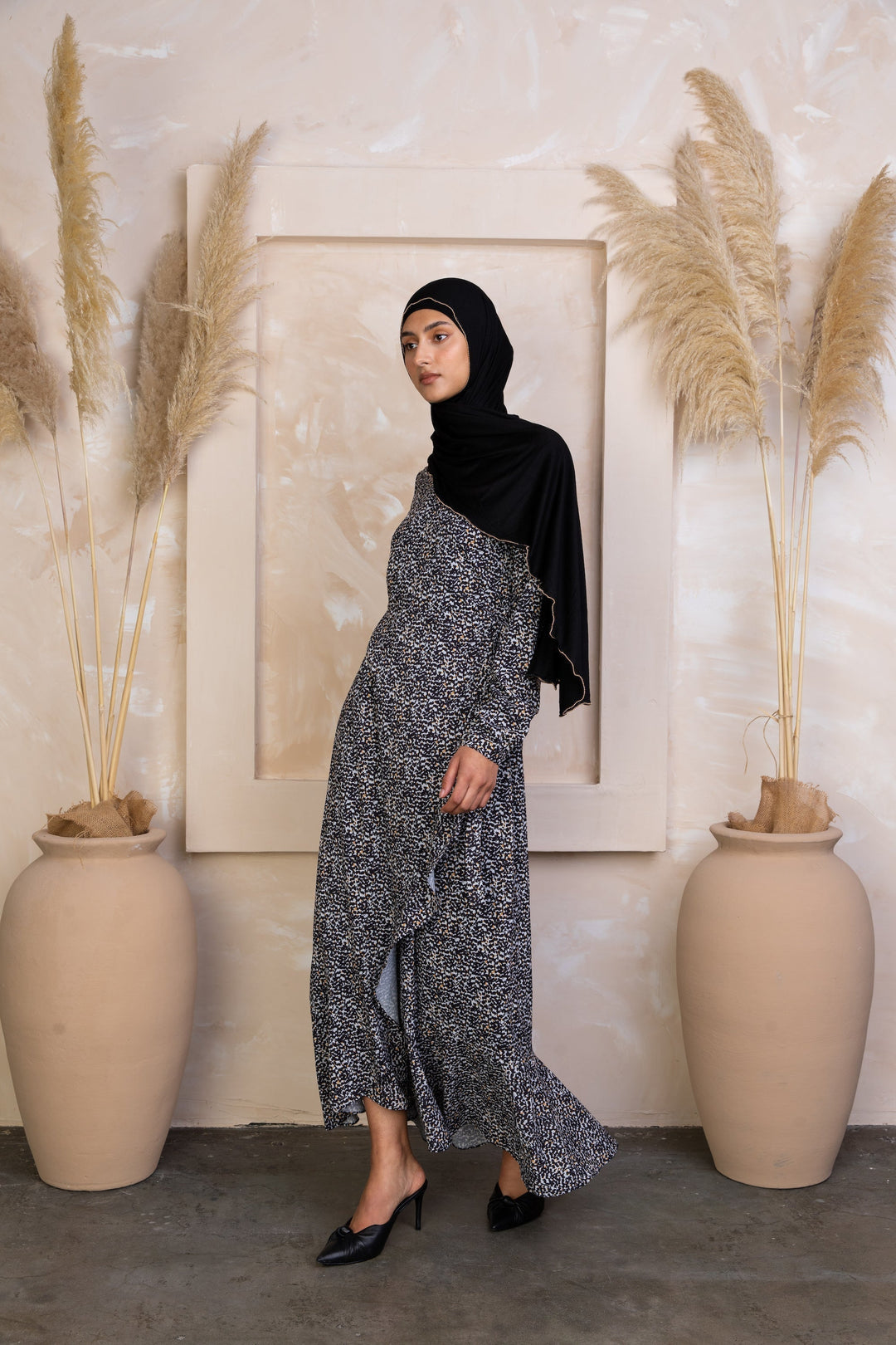 Woman in a patterned dress and black hijab wearing a yellow ruffle wrap dress maxi