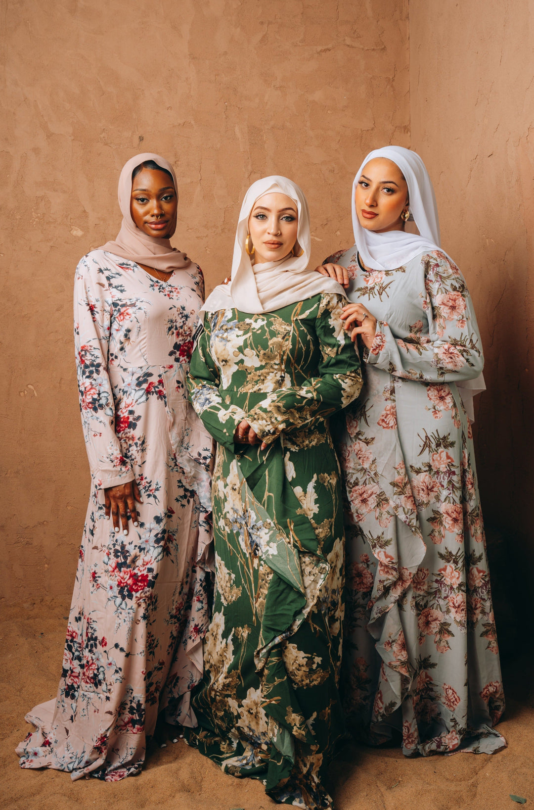 Three women in floral maxi dresses with hijabs featuring blush pink ruffle designs