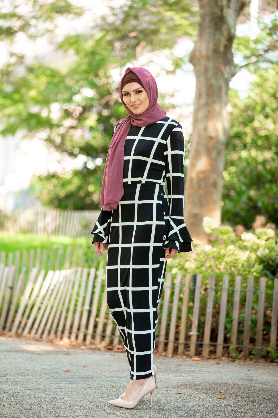 Woman in black and white grid dress with maroon hijab and brown criss-cross underscarf