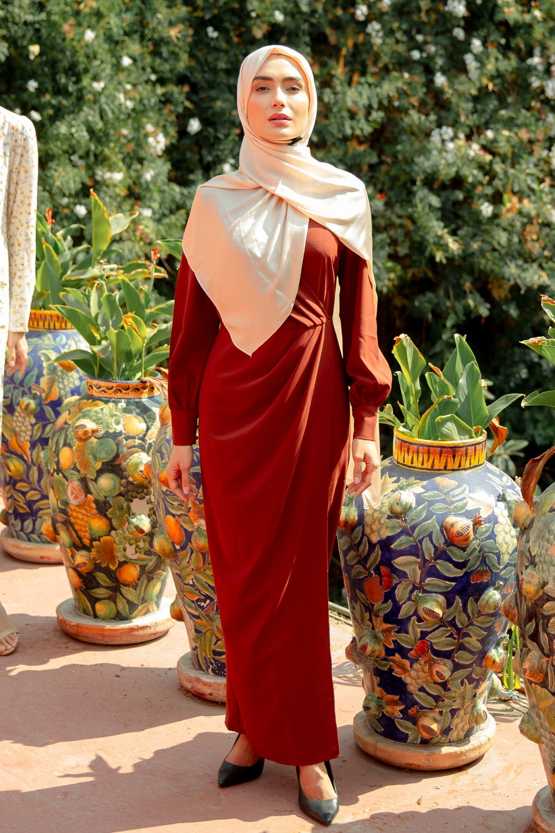 Woman in a rust-colored brown wrap maxi dress with criss cross neckline and light hijab