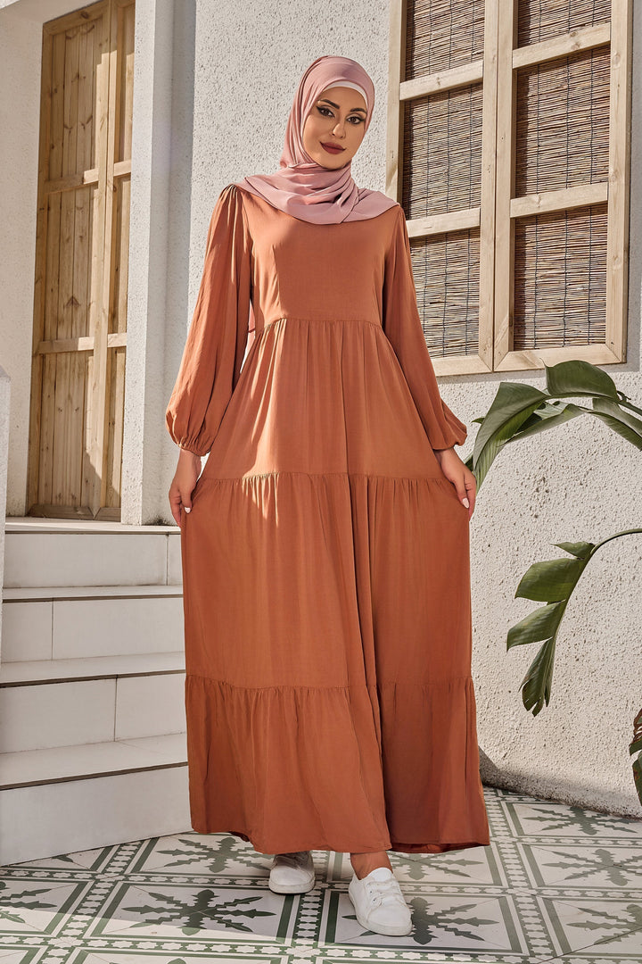 Woman in a burnt orange long sleeve maxi dress with pink hijab, showcasing style and elegance