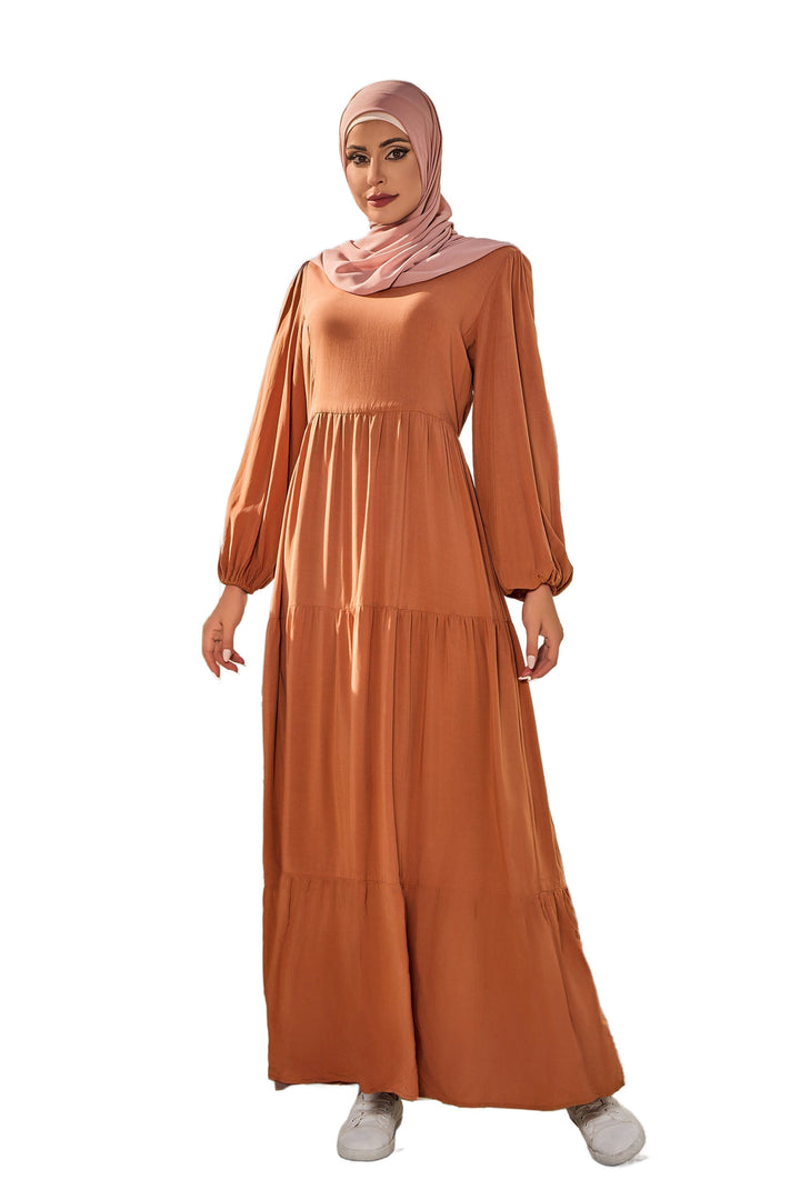 Woman in a brown tiered dress and pink hijab wearing a burnt orange long sleeve maxi dress