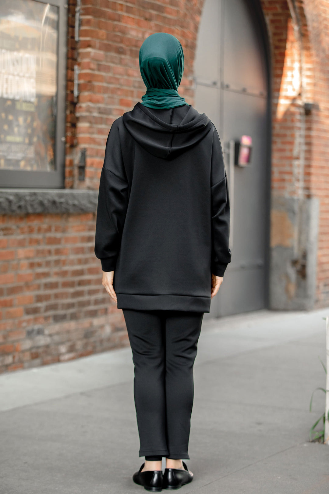 Woman wearing a black hoodie sweatshirt and green hijab in a pants set