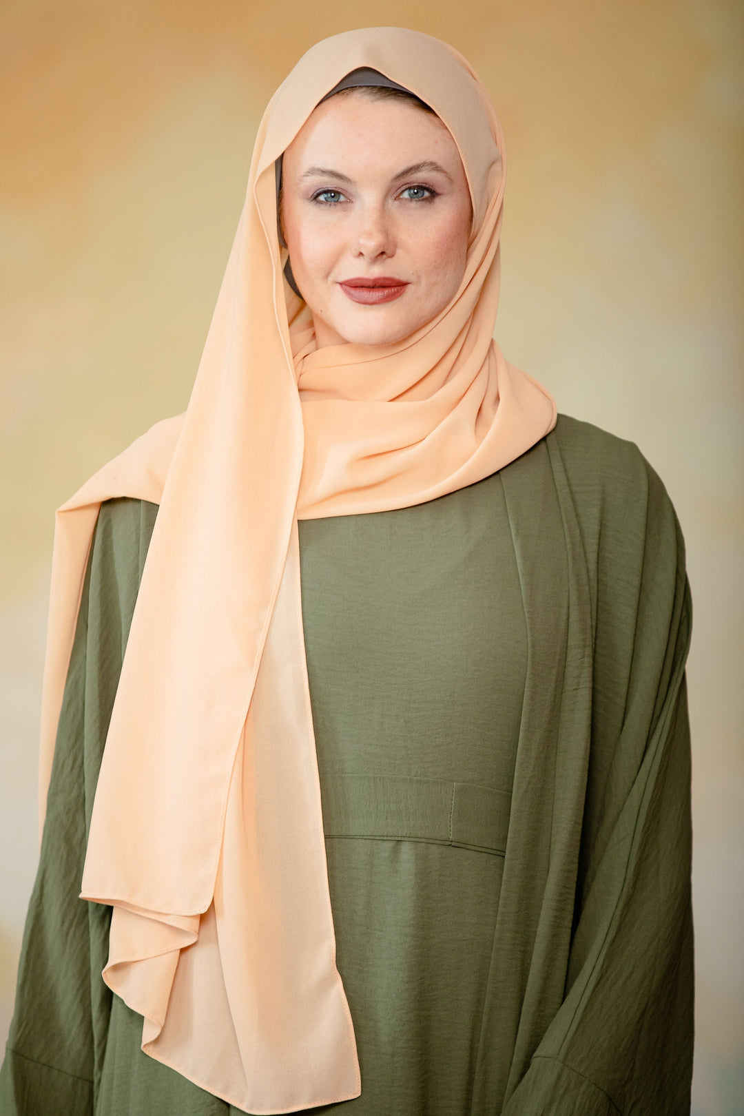 Woman in a peach chiffon scarf with an olive green dress, showcasing elegant style