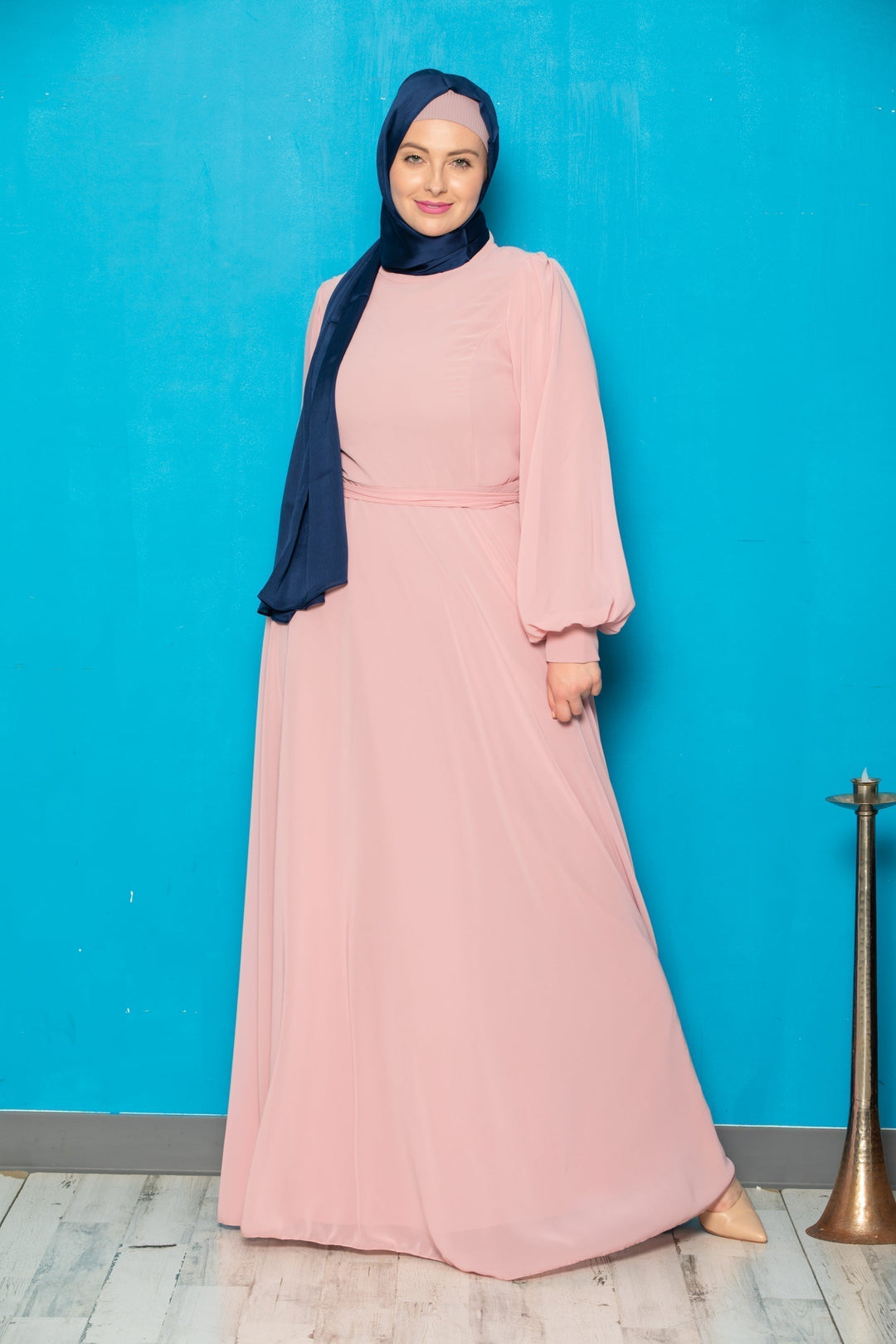 Woman in a long pink chiffon long sleeve gown with a blue hijab and belt included