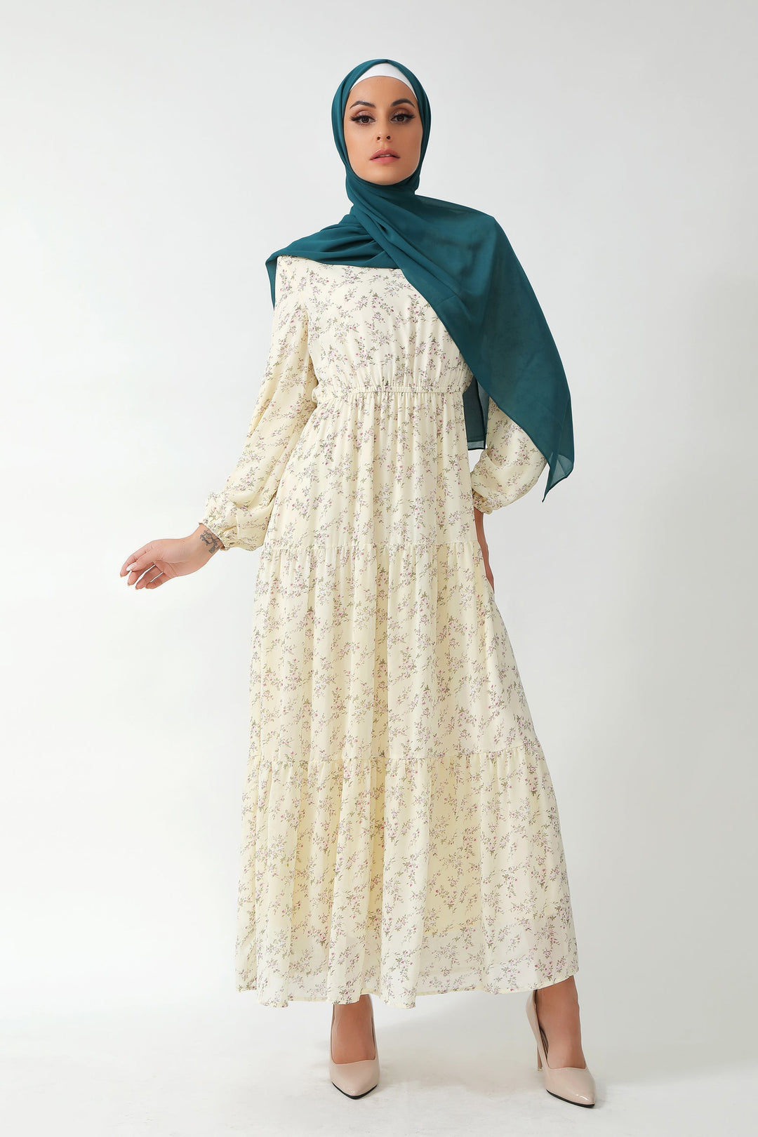 Woman in a cream floral tiered maxi dress and teal hijab showcasing elegant style