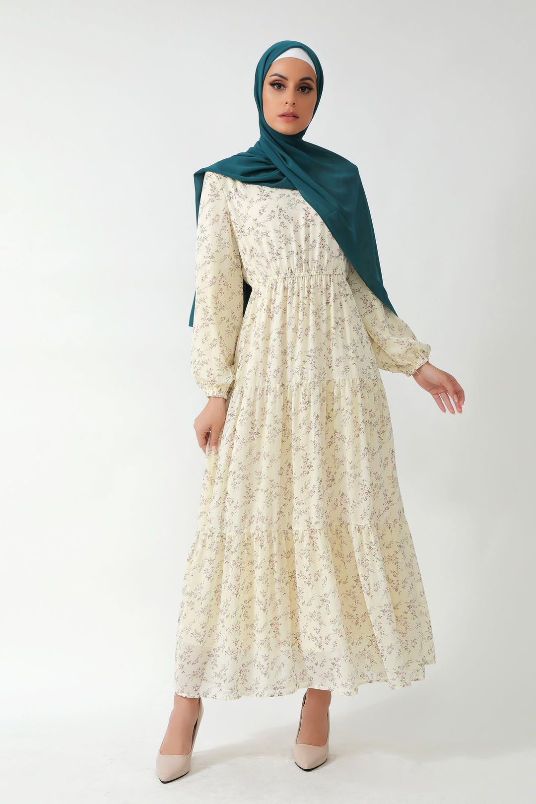 Woman in cream floral tiered maxi dress with green hijab, showcasing floral elegance