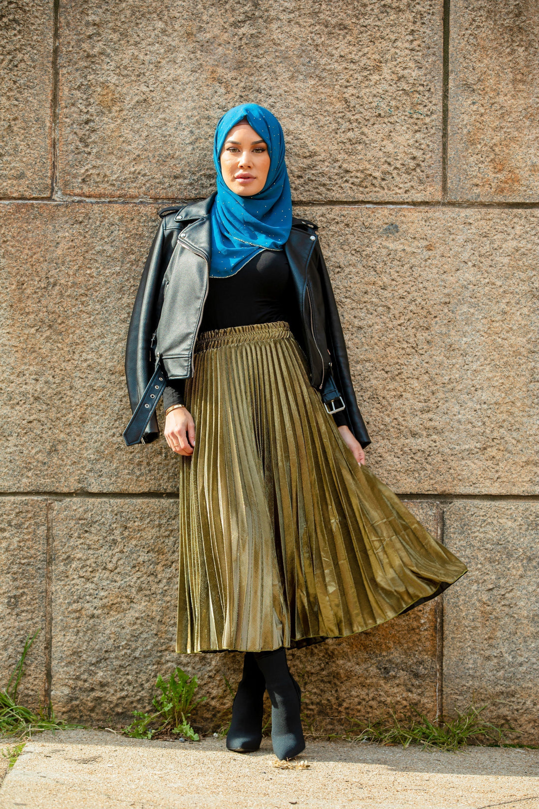 Woman in hijab wearing a leather jacket and gold metallic pleated chiffon maxi skirt