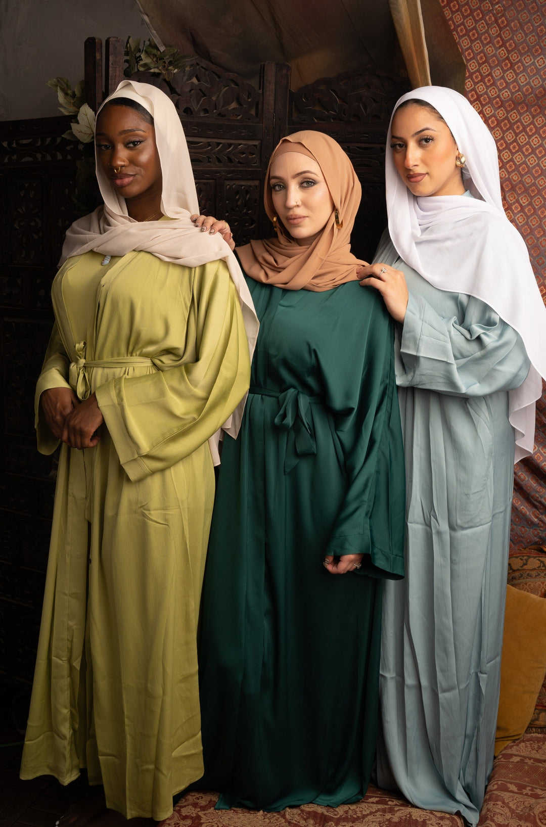 Three women in modest green sleeveless dress and open abaya set showcasing stylish elegance