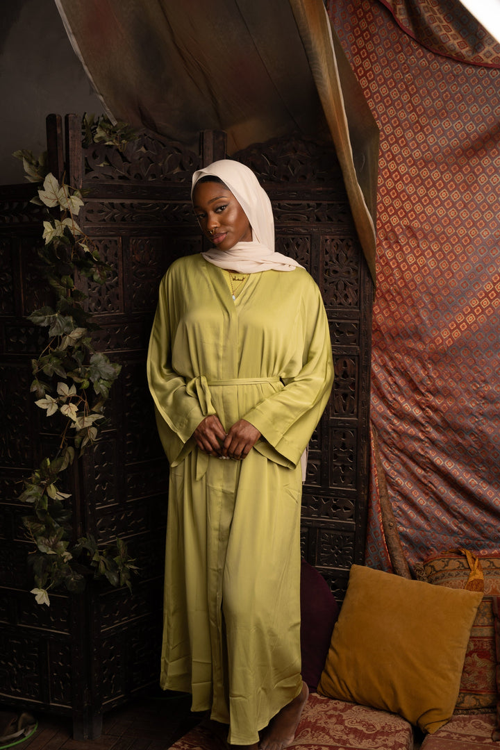 Woman in a long green dress and hijab showcasing the Grass Green Sleeveless Dress and Open Abaya Set