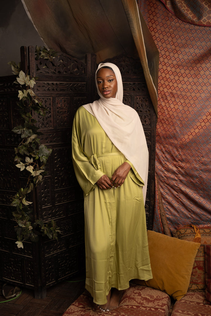 Woman in a light green dress and hijab modeling an open abaya and green sleeveless dress set