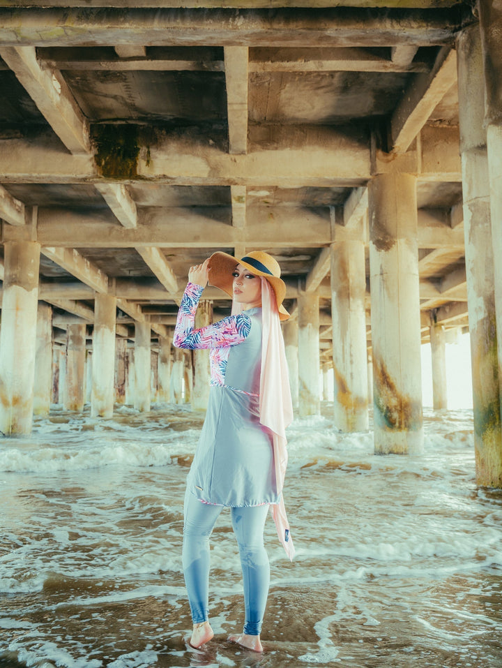 Woman in gray floral 3 piece modest swimsuit relaxing under a pier