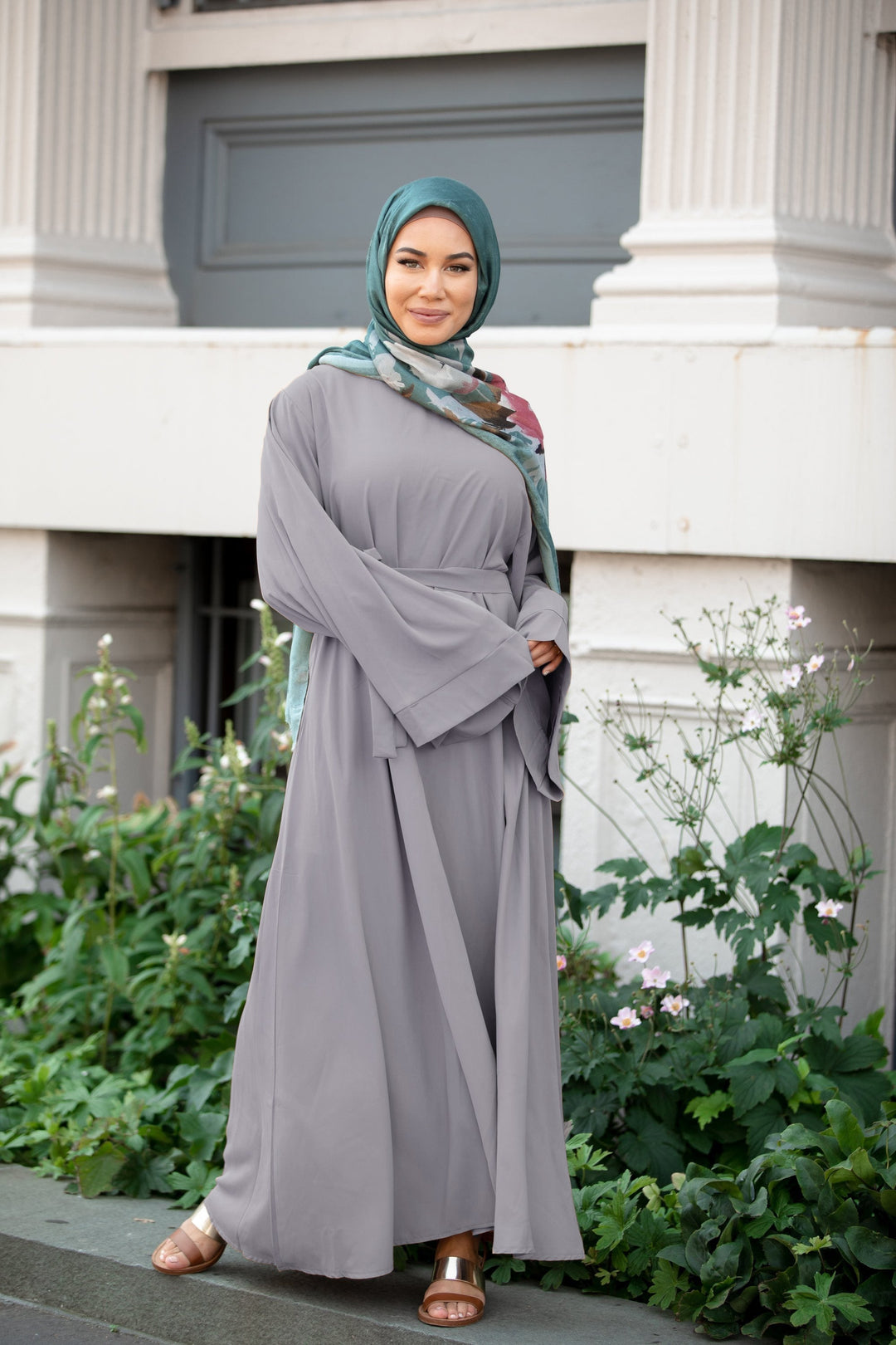 Woman in gray kimono sleeve abaya maxi dress with fabric tie belt and teal hijab