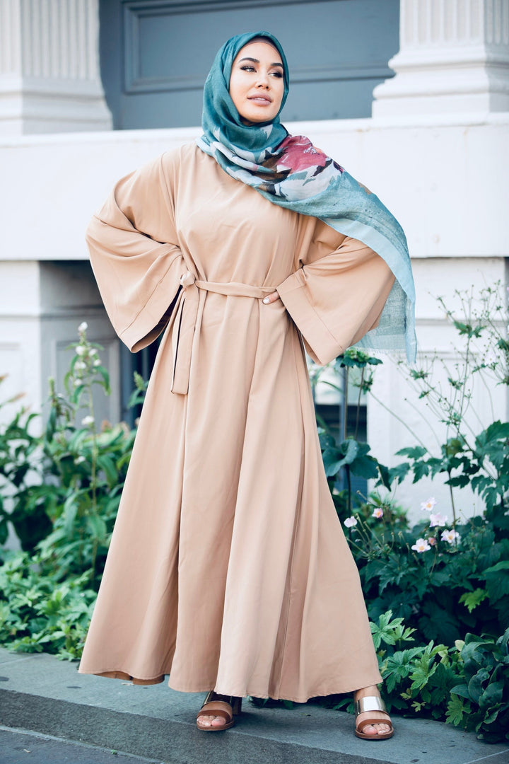 Woman in tan maxi dress with kimono sleeves and fabric tie belt, wearing teal hijab