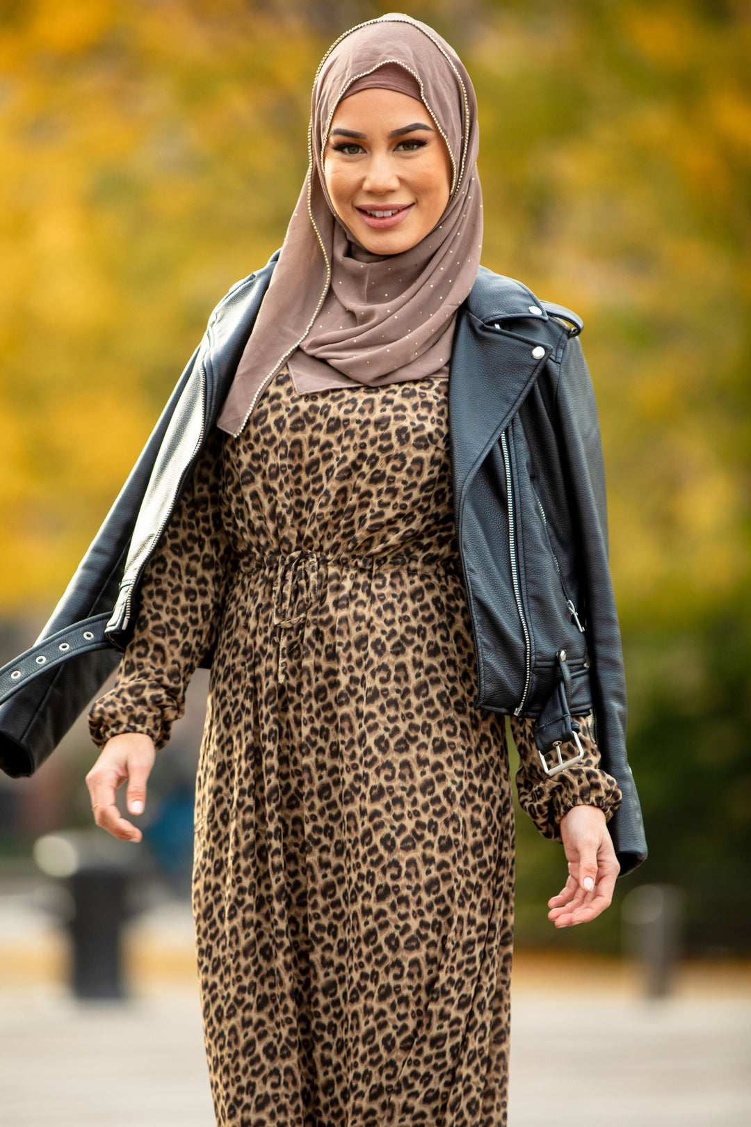 Woman in leopard print maxi dress with leather jacket and hijab, featuring elastic cuffs