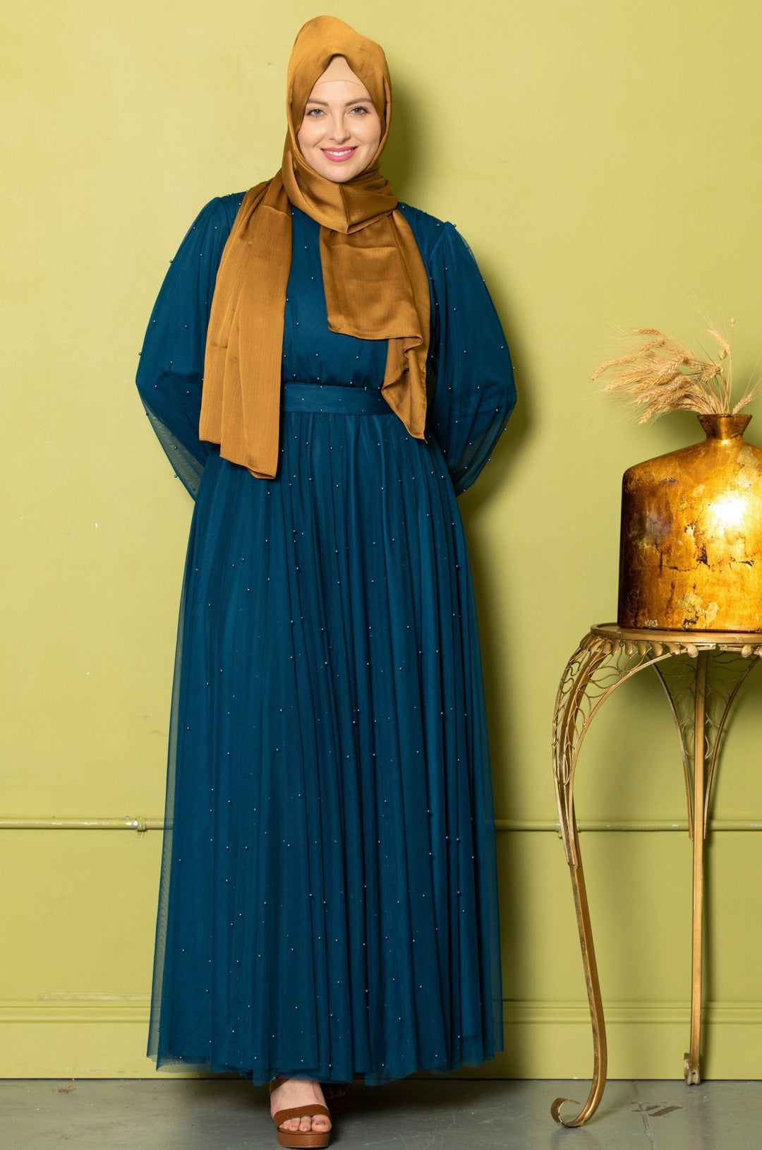 Woman in teal Mesh Pearl Long Sleeve Gown with a gold hijab, showcasing elegance