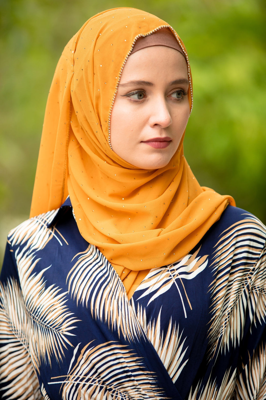 Woman in a mustard chiffon hijab and navy shirt with palm leaves, showcasing style